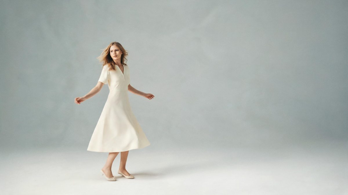A woman in a simple dress on a seamless studio backdrop with her arms slightly out as if caught mid-rotation