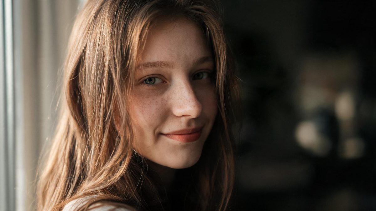 A European woman smiling lightly in natural window light, freckles across her nose, soft background, no text anywhere