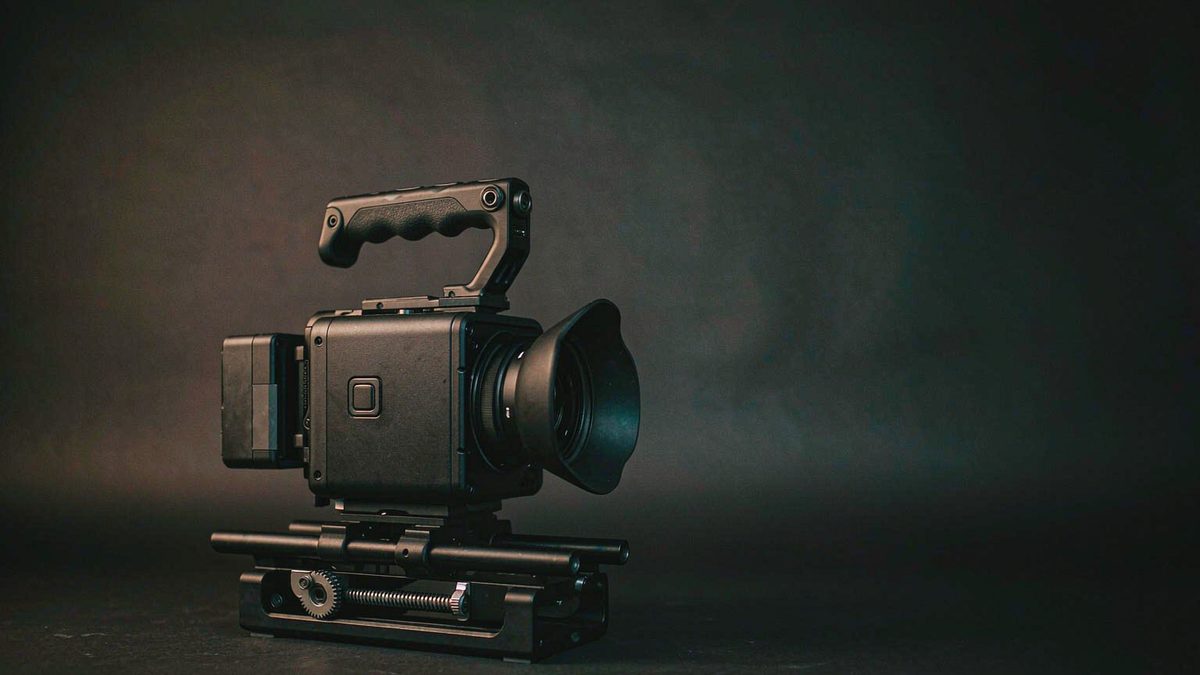 A compact cinema camera mounted on a short motorized slider on a dark charcoal surface, lit by a warm key light from the left