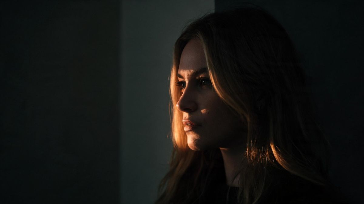 A dim corner of a portrait with one warm light running along an edge of the face, the rest of the frame in deep shadow