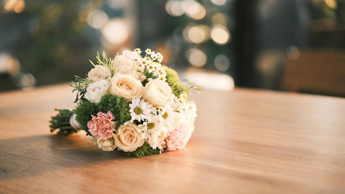 A gathered bouquet of soft flowers lying on a wooden table in daylight, no person