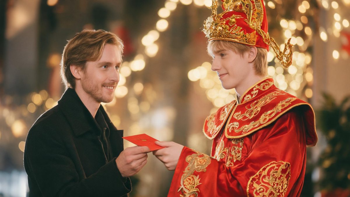 A man receiving a red envelope from a traditional Chinese God of Wealth figure in red and gold painted robes