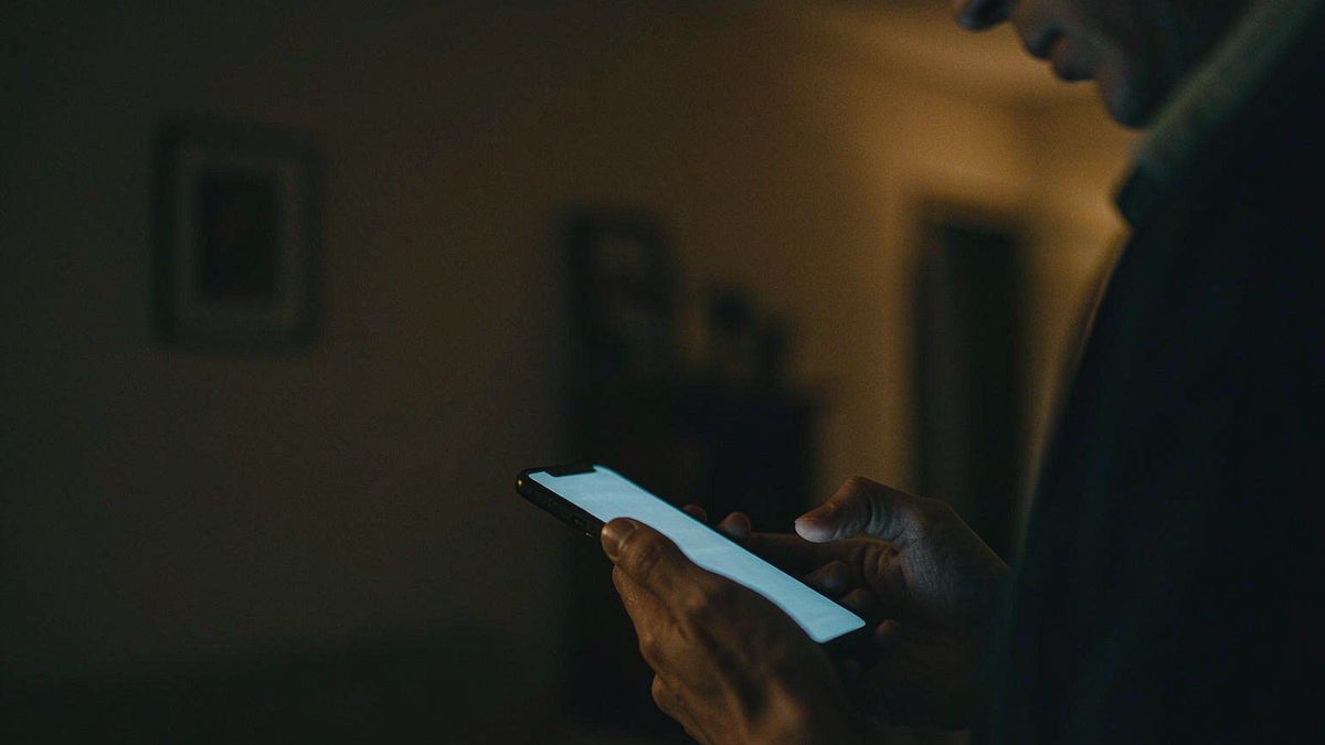 A person holding a phone with a glowing screen in a dark room