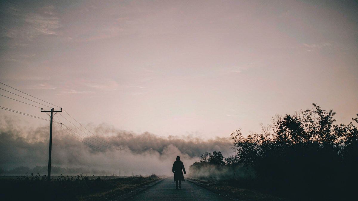 A lone figure walking away down a fogged road at dusk