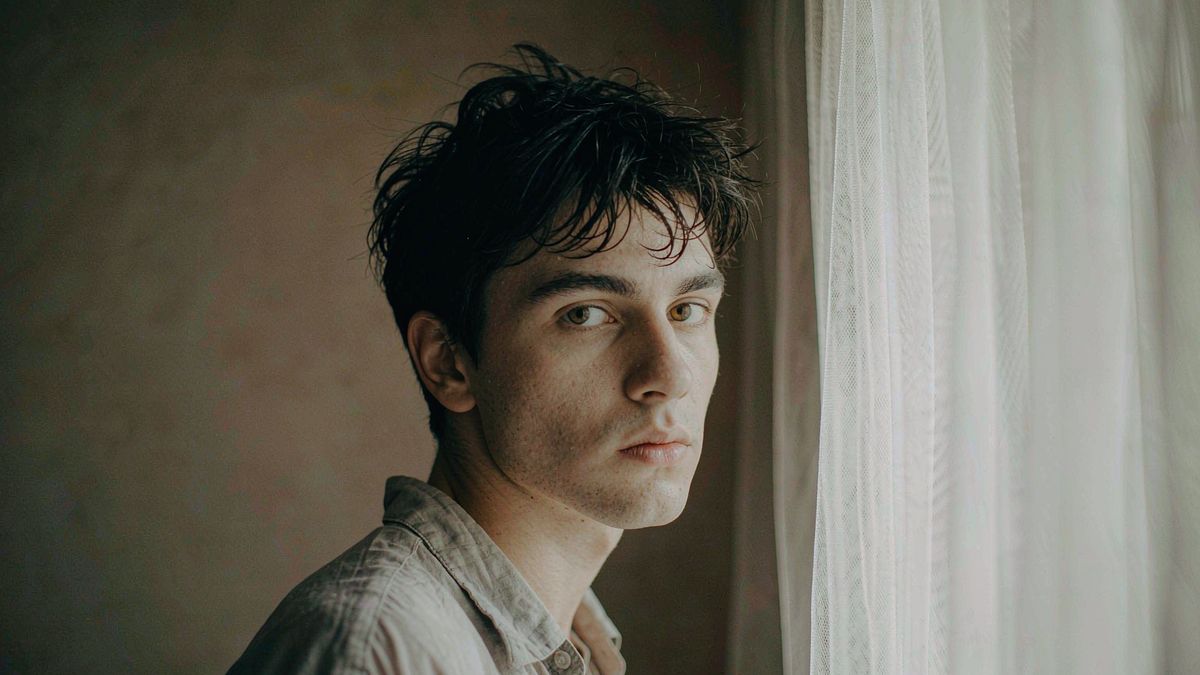 A portrait of a person against a plain warm grey wall in soft window light
