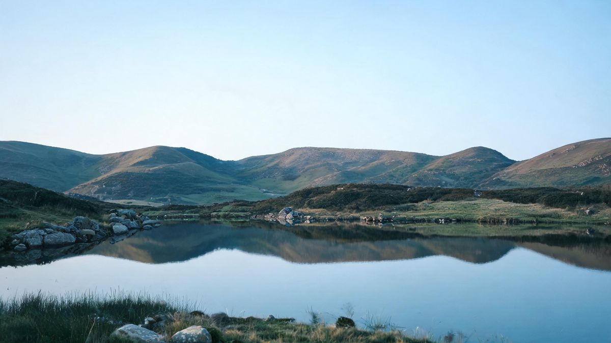 A still lake mirror-reflecting hills in cool morning light.