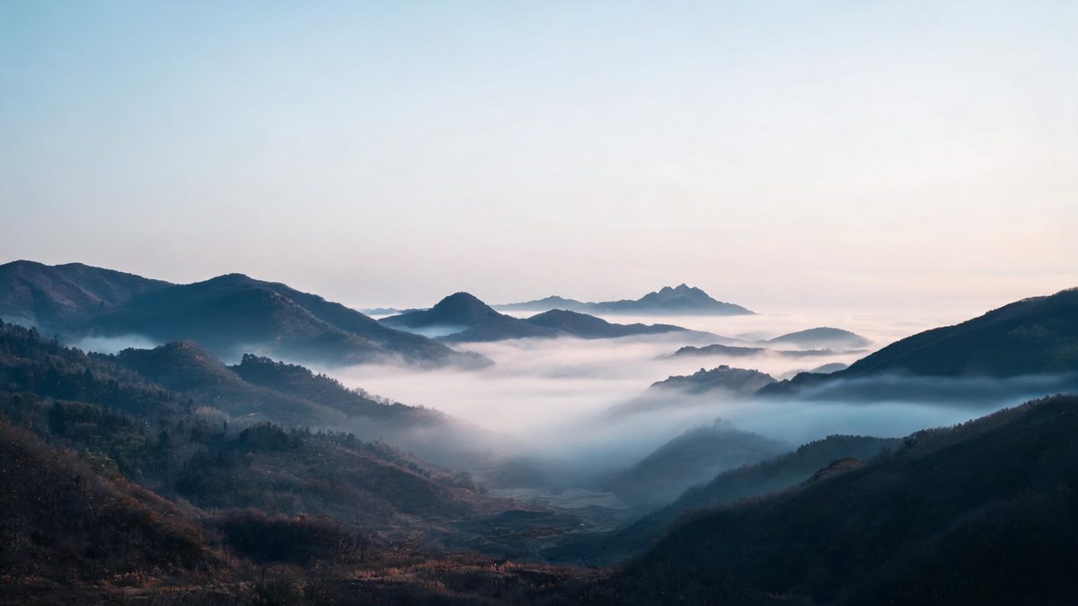 Layered mountain peaks in morning mist, soft cool light, a wide quiet scene.