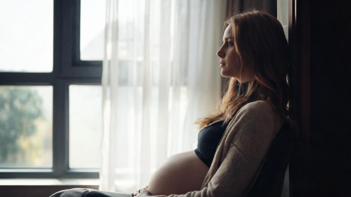 A maternity portrait in profile by a window, a sheer curtain behind, calm mood.