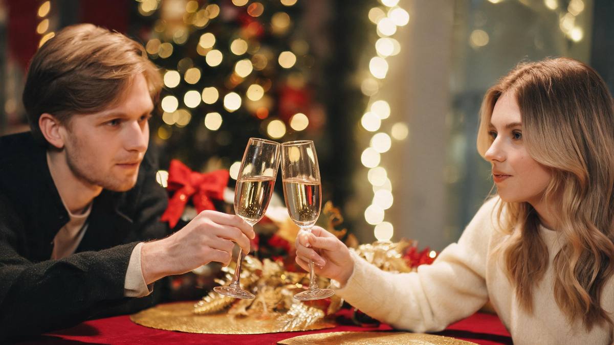 A festive table setting with two champagne flutes raised and warm bokeh lights behind