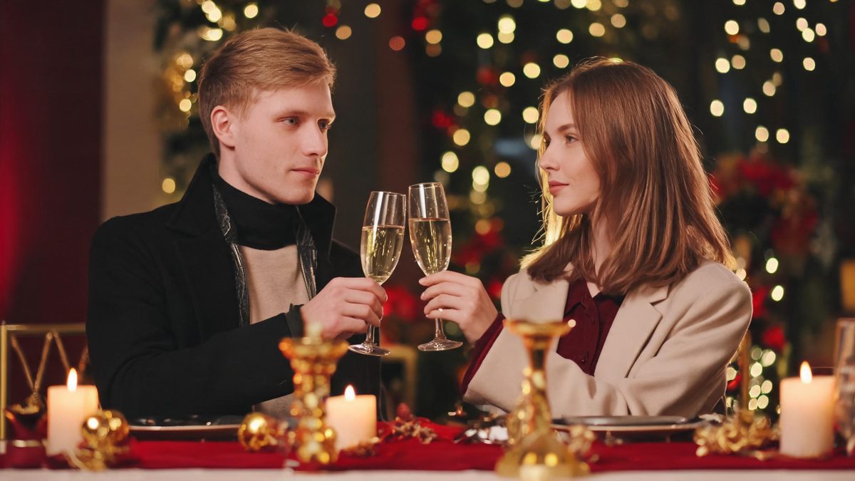 A man and a woman raising champagne flutes towards each other at a festive table in warm golden light