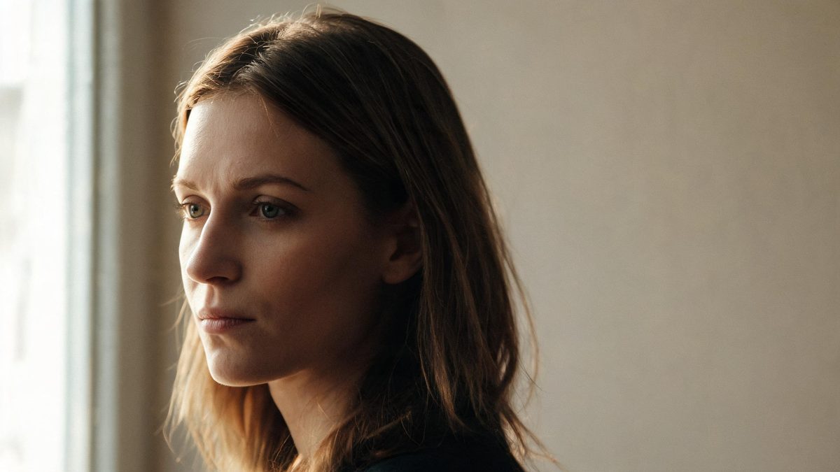 A person lit by soft window light, half-turned toward the light with the other side in gentle shadow.