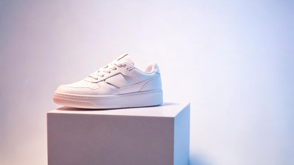 An unbranded white sneaker on a pedestal lit by soft pink and blue gradient studio lights.
