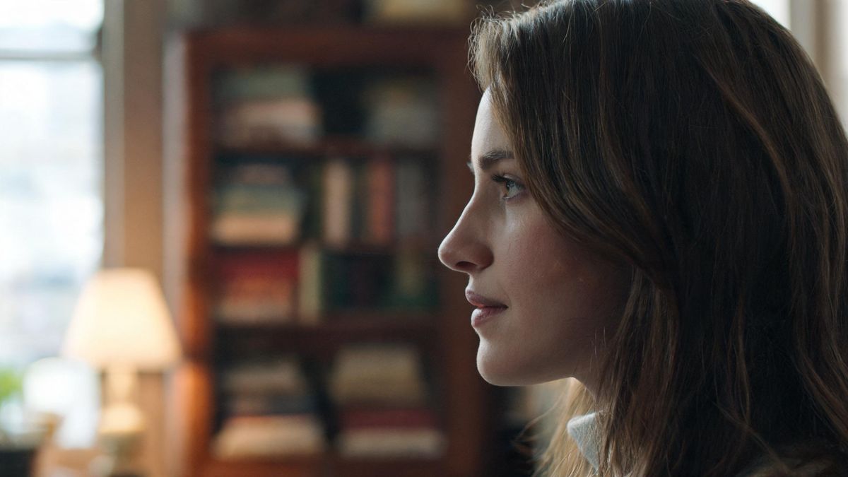 A profile portrait with a blurred bookcase behind, warm light, approachable mood.