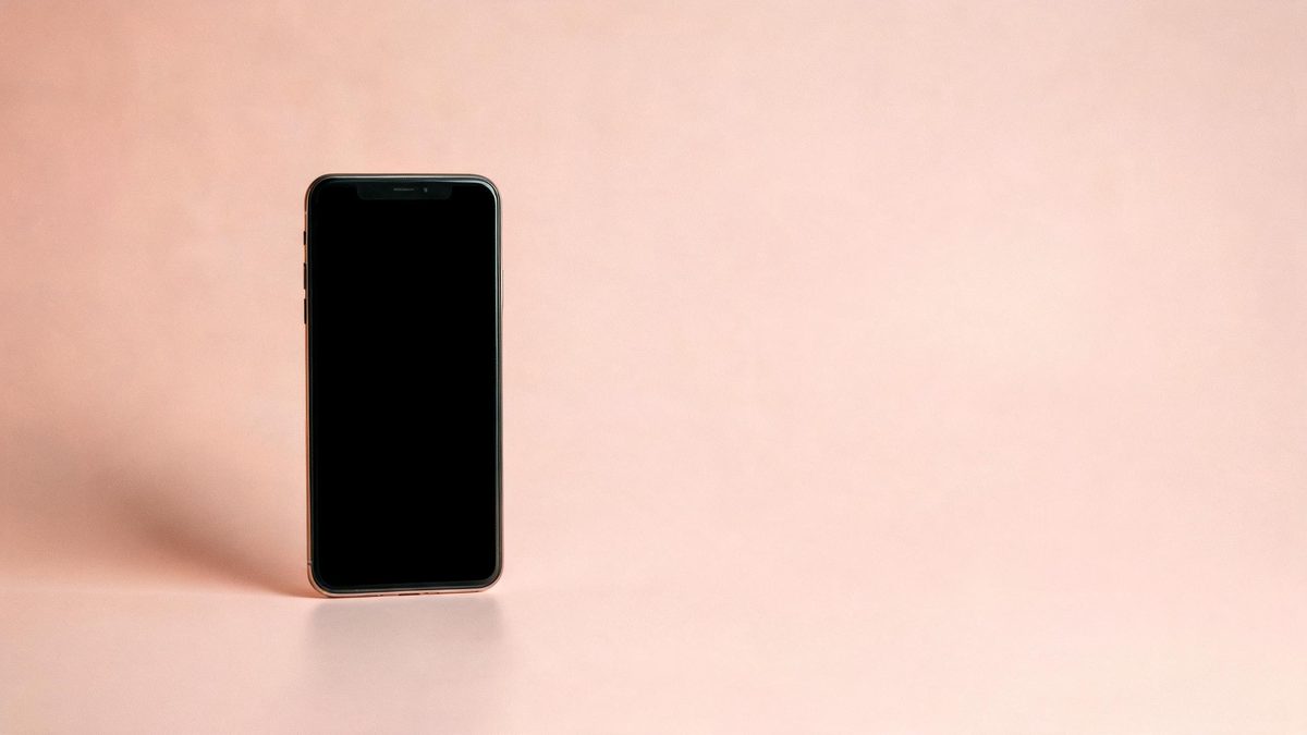 A vertical smartphone with a blank screen standing on a pastel background, minimal studio composition.