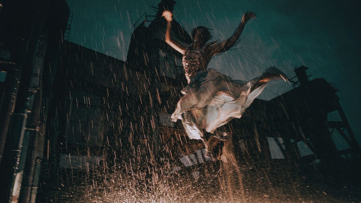 A dancer mid-leap in heavy rain against a dark industrial skyline