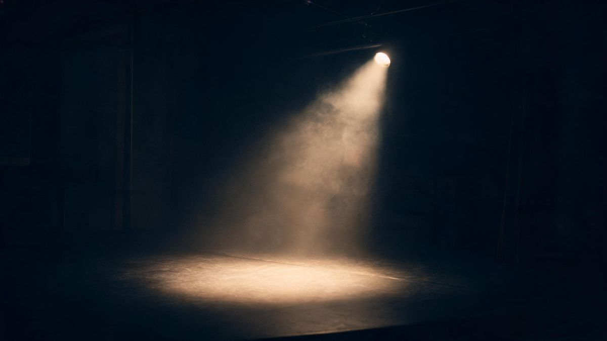 A dark studio stage lit by a single spotlight with soft haze, empty and atmospheric.