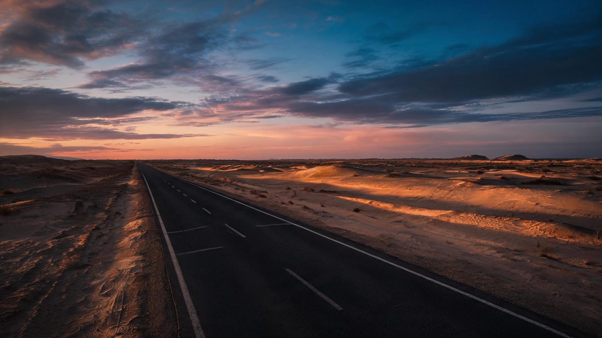 An empty desert highway at dusk with long shadows and a vast sky, cinematic atmosphere, no people.