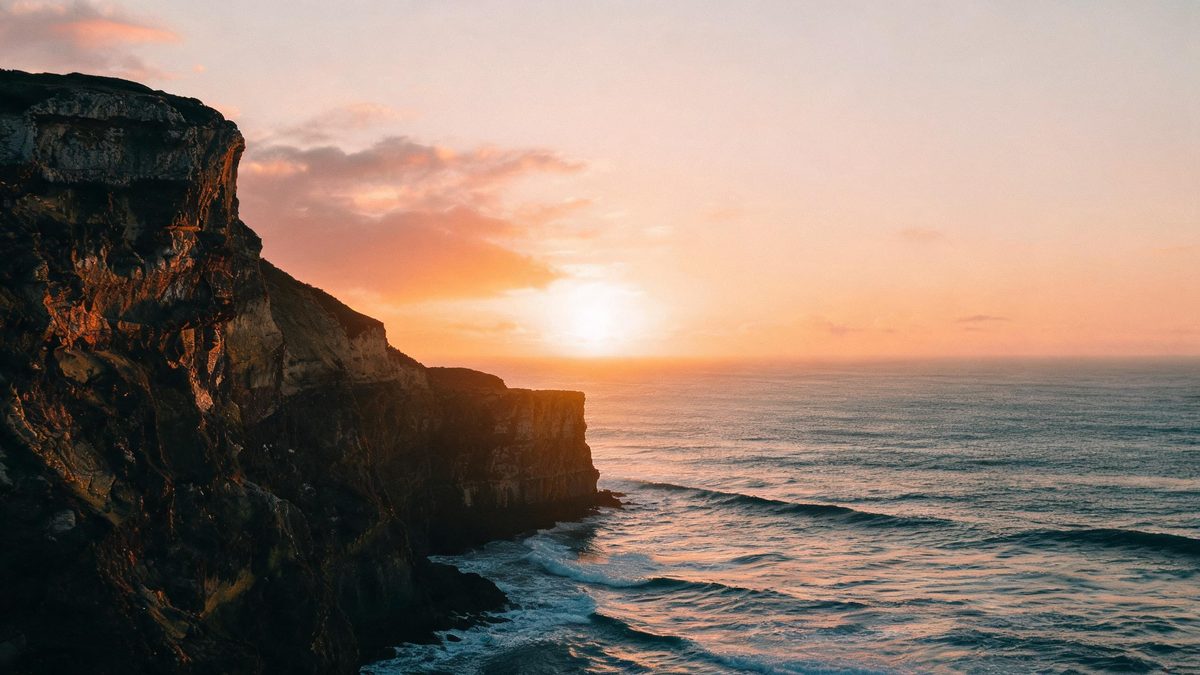 A coastline cliff at golden hour, the sea below, soft warm light, wide composition, no people in focus.