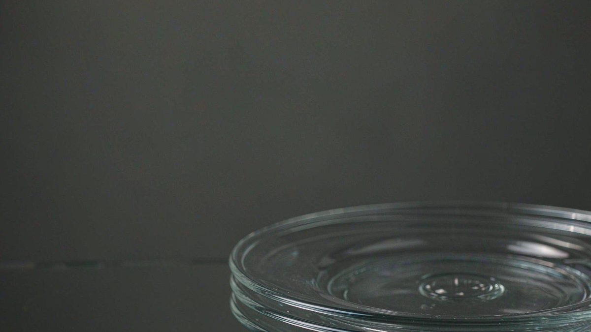 A stack of clear glass plates slightly misaligned so the edges double, under cool diffused light on a dark background