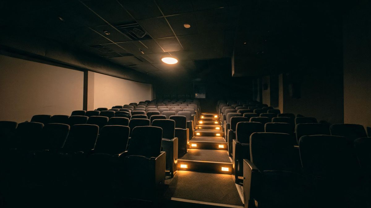 Rows of empty seats in a small cinema lit by one ceiling fixture, the aisle lights receding