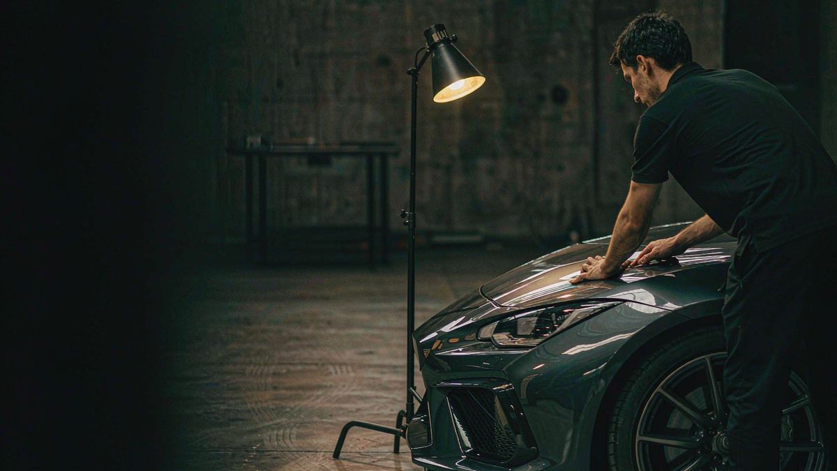 A detailer working on a dark car under a warm work lamp in a concrete garage