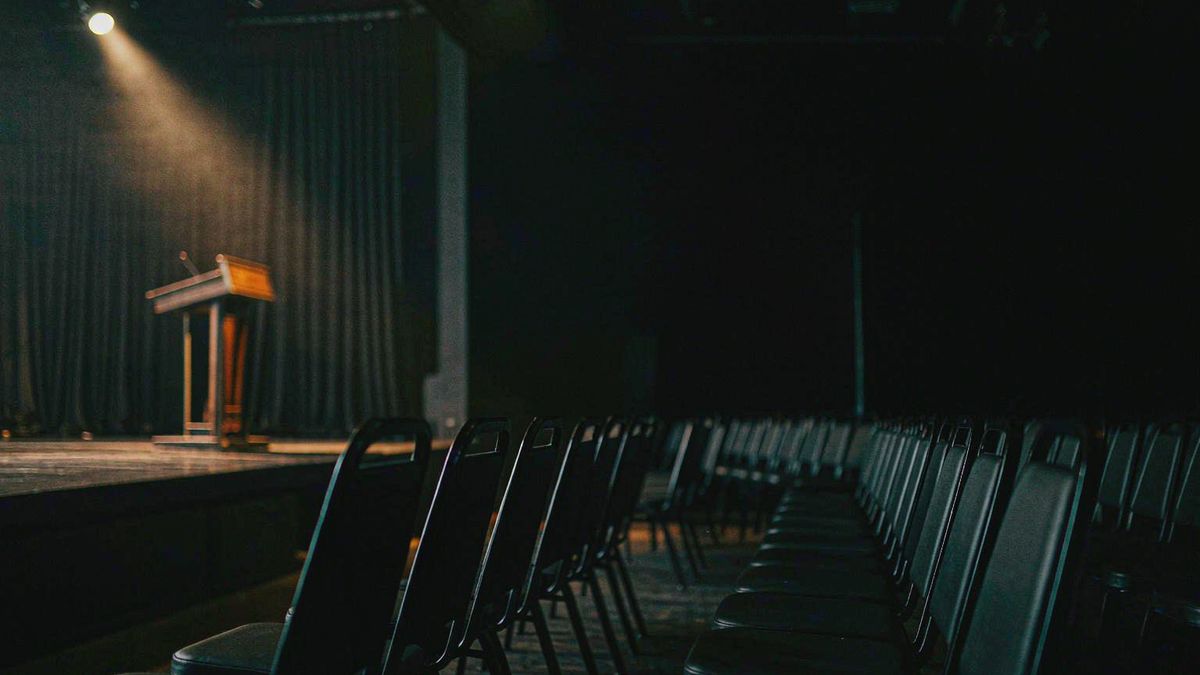 Empty conference seating with a single spotlight on an unoccupied stage
