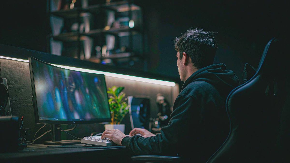 A player seen from behind facing an ultrawide monitor in a dark room