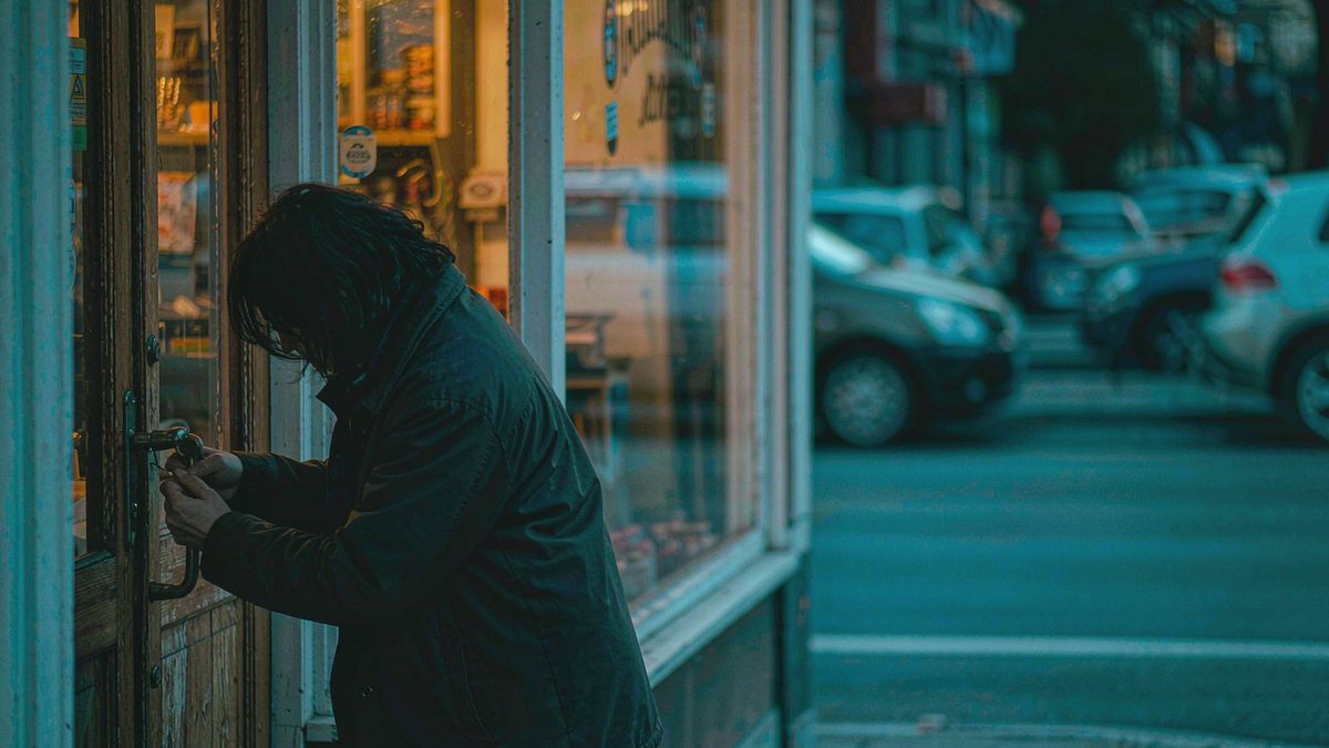 A shopkeeper unlocking a storefront at opening as light spills onto the pavement