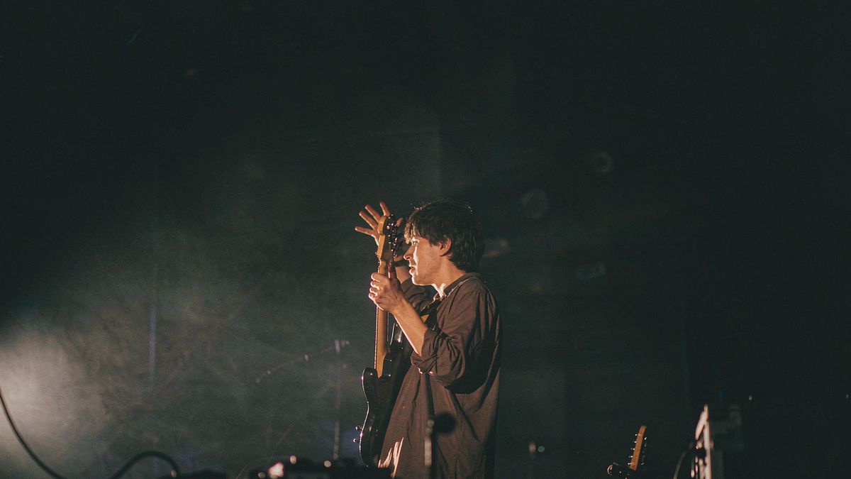 A musician with a guitar alone under a single warm light on a dark stage