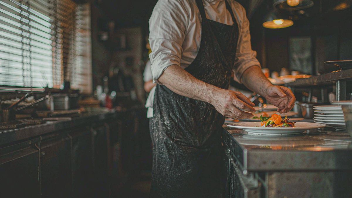 A plated dish being set down at a dark restaurant pass