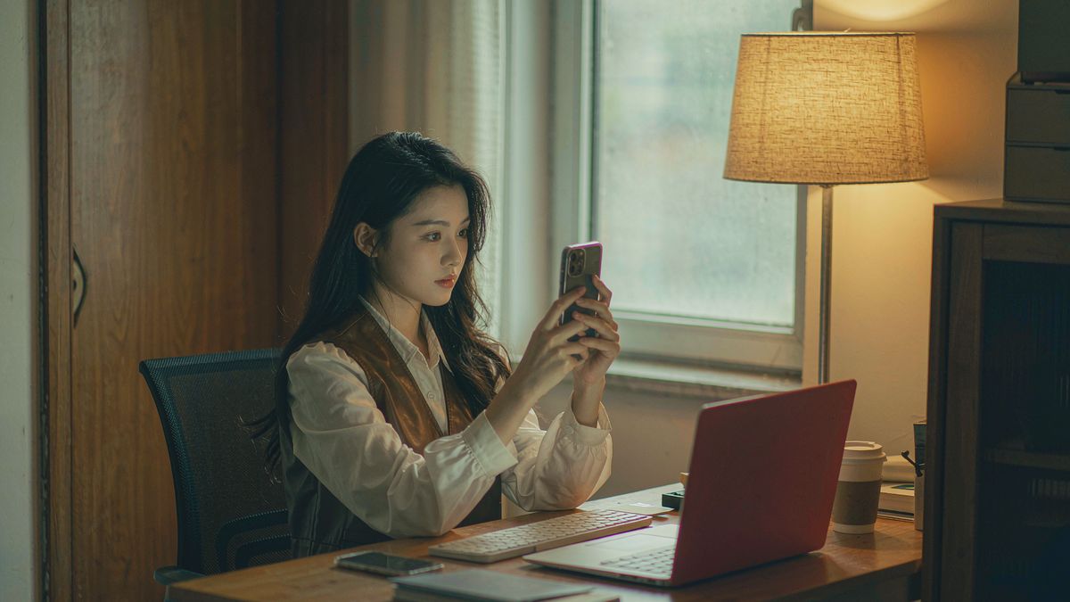 A person filming a short video message at a desk lit by a warm lamp