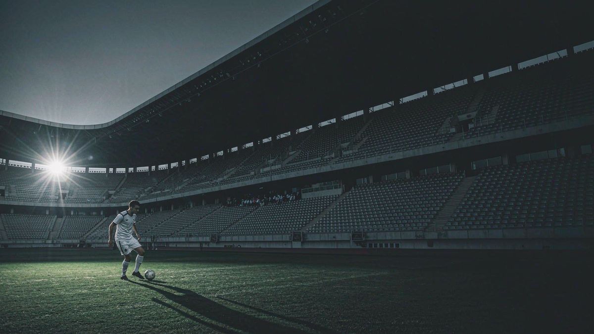 A football player striking a ball on a floodlit pitch at dusk