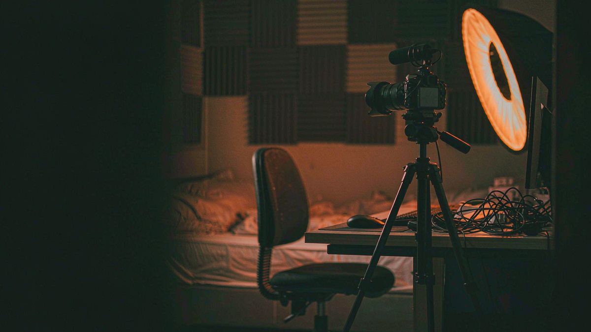 A camera on a tripod facing an empty chair in a small studio set