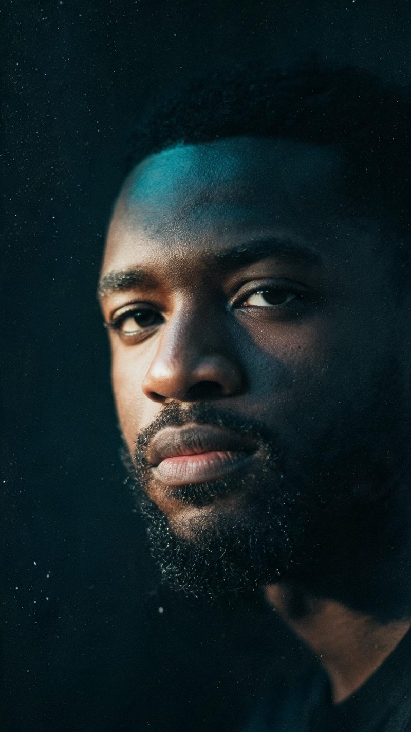 Cinematic close-up portrait of a man with dark skin and a short beard under hard side light with teal shadows