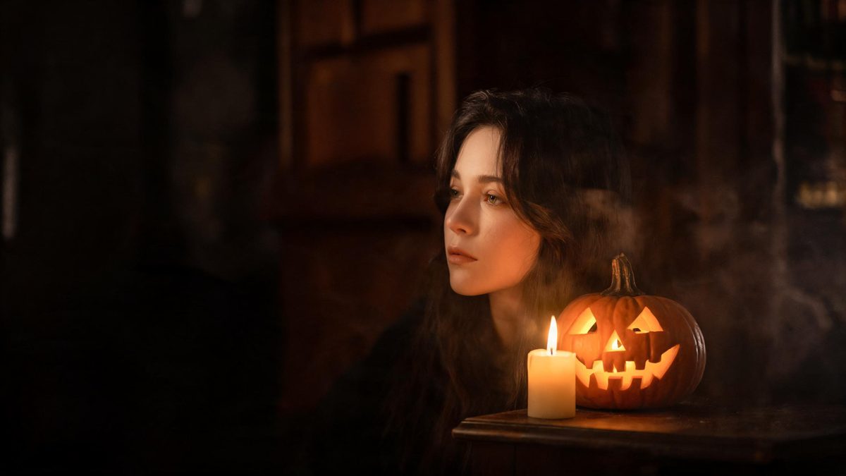 Moody autumnal portrait lit by candlelight and the warm glow of a carved pumpkin in a dark interior