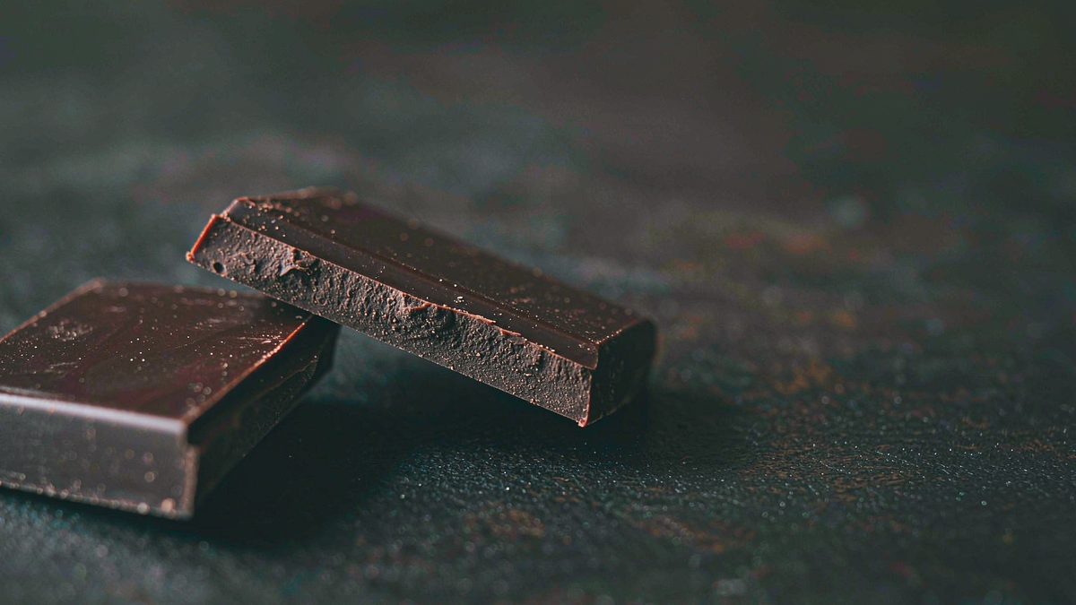 A snapped bar of chocolate showing a matte broken edge over a dark cloth, split open at the moment of the cut