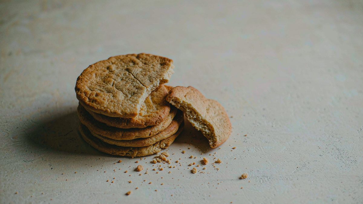 A stack of thin biscuits with a clean broken edge and scattered crumbs, broken apart at the moment of the cut