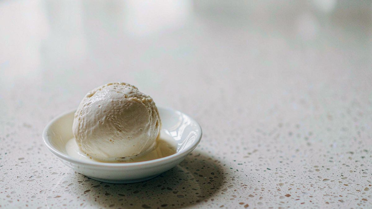 A scoop of soft ice cream on a small dish with condensation catching the light, split open at the moment of the cut
