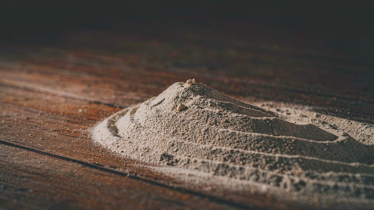 A heap of damp sand on a flat surface with fine texture and small ridges, split open at the moment of the cut