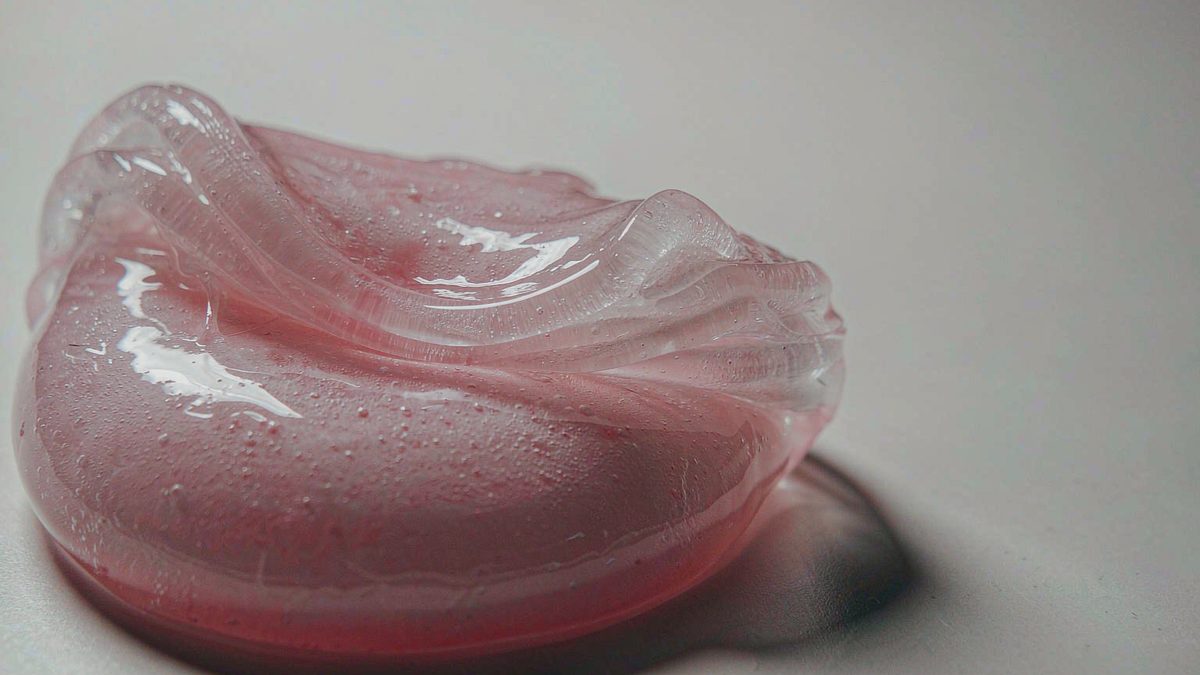 A glossy blob of soft putty being pressed on a clean white surface, split open at the moment of the cut