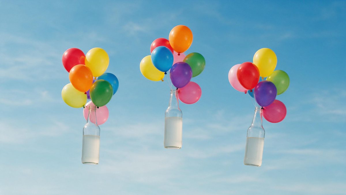 Three plain beverage bottles floating in the air held up by clusters of balloons against open sky