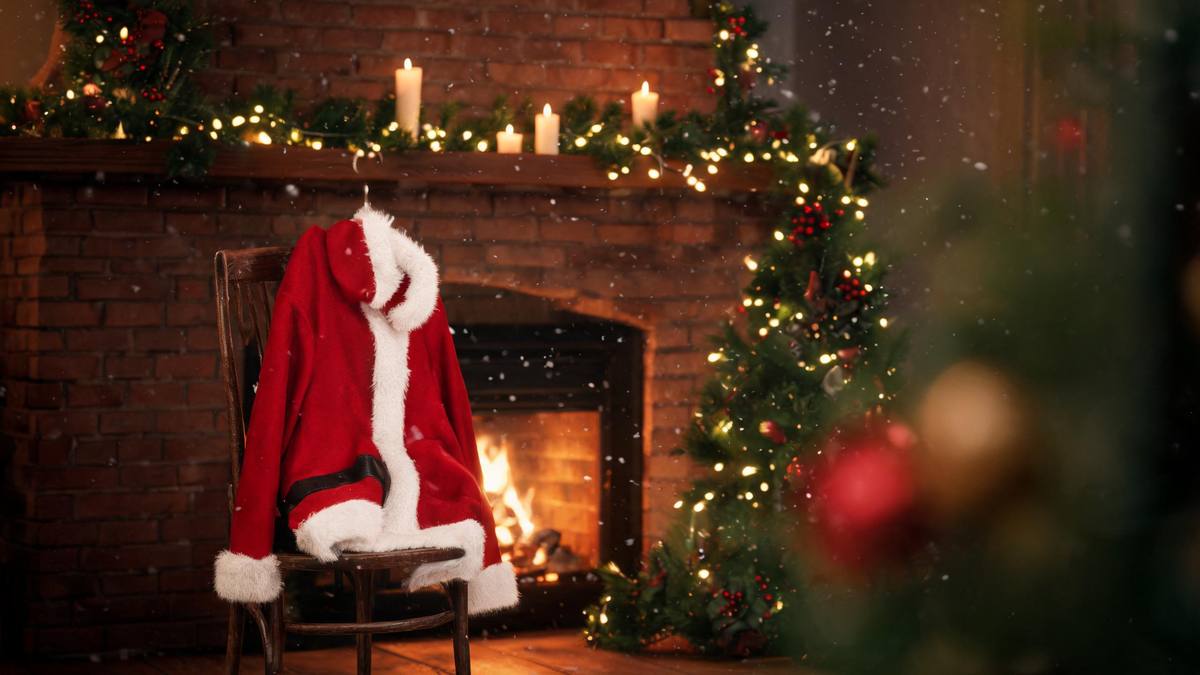 A red Santa coat with white fur trim hanging over the back of a wooden chair beside a fireplace