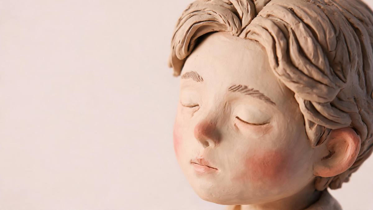 Close-up of sculpted clay hair and a painted clay face on a small figurine on a pastel backdrop