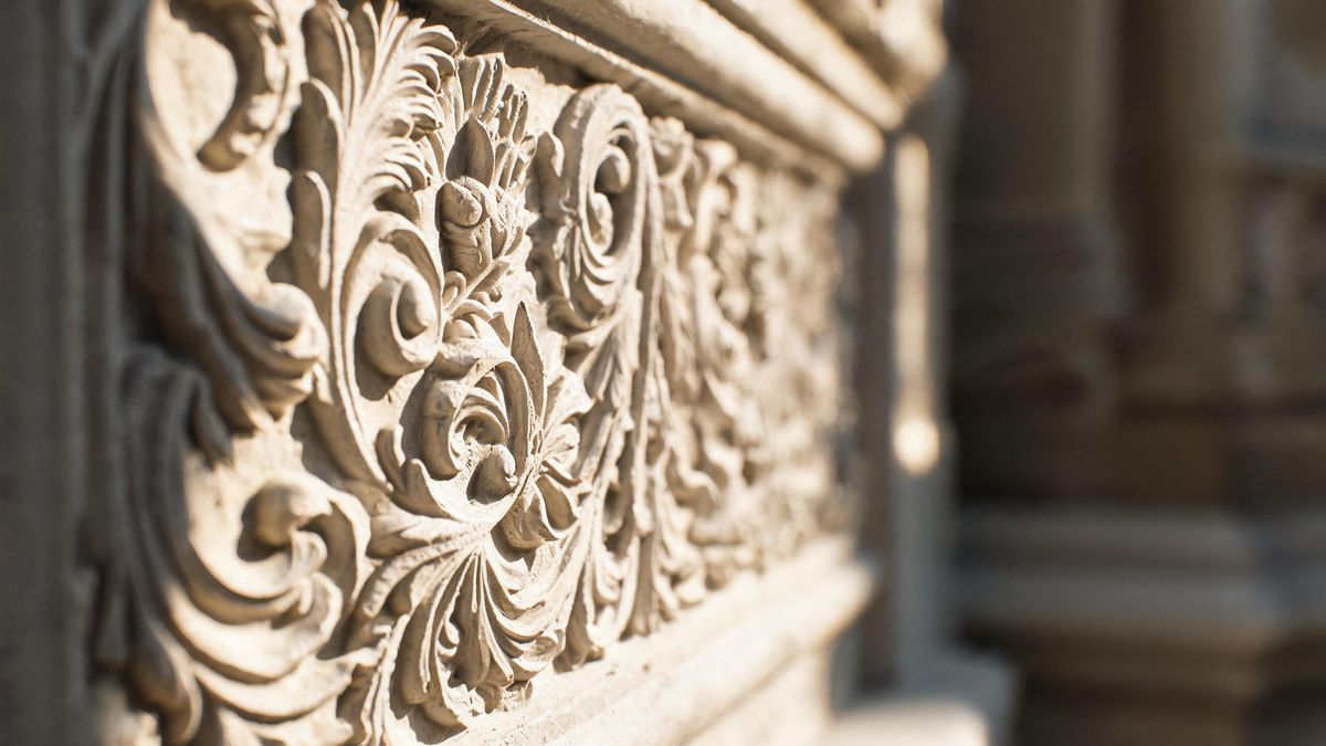 Close-up of a carved plaster surface with fine relief detail under raking light from the left