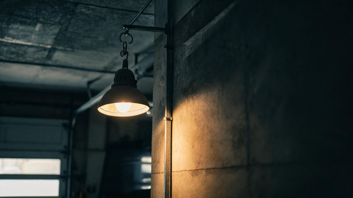 A dim garage interior with a work lamp hanging on a hook, the concrete walls falling into darkness