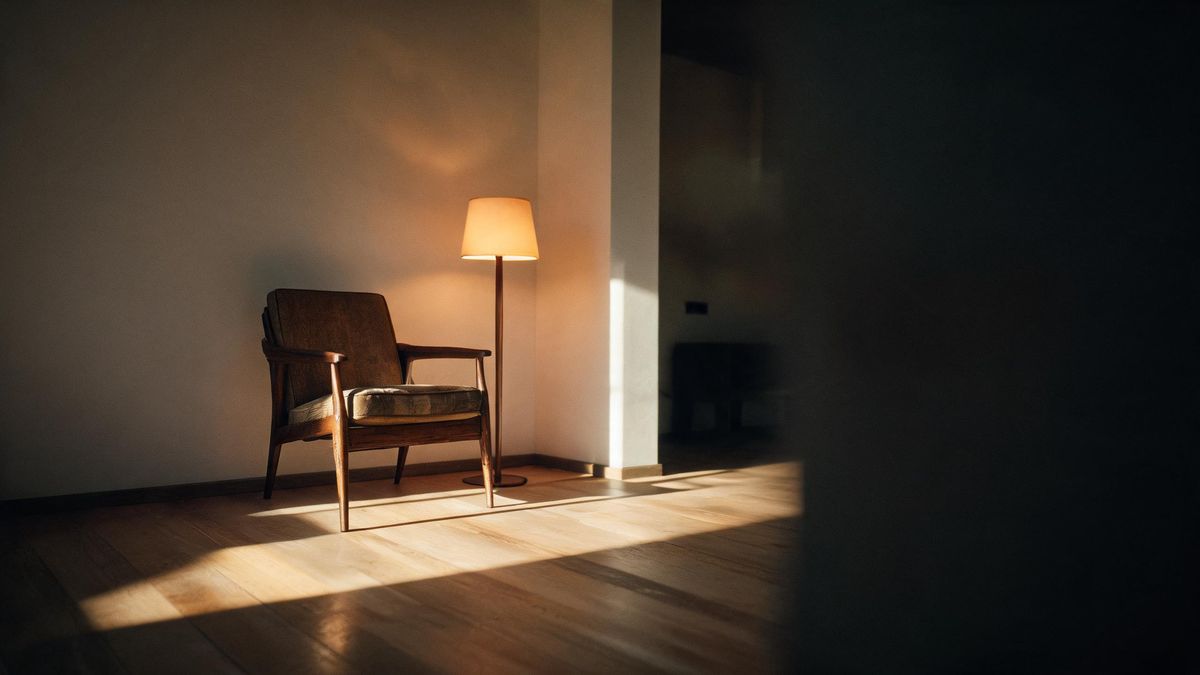 A sunlit corner of an empty room with a wooden chair and long shadows stretching across a bare floor