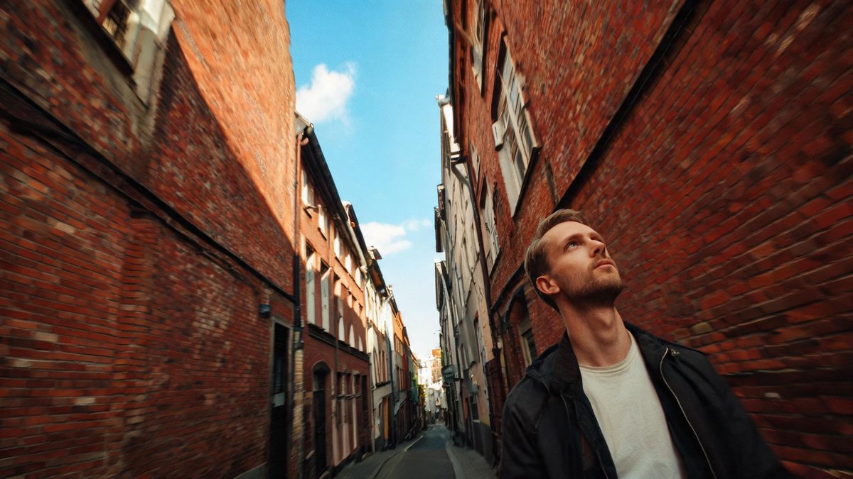 An extreme fisheye view of a man in a narrow city street with brick walls bending inward at the frame edges