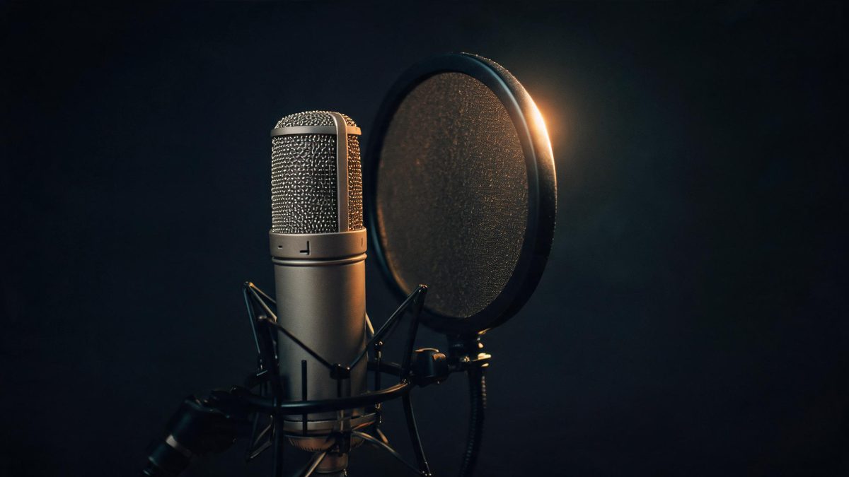 A studio condenser microphone with a black pop filter lit from behind by a single warm rim light