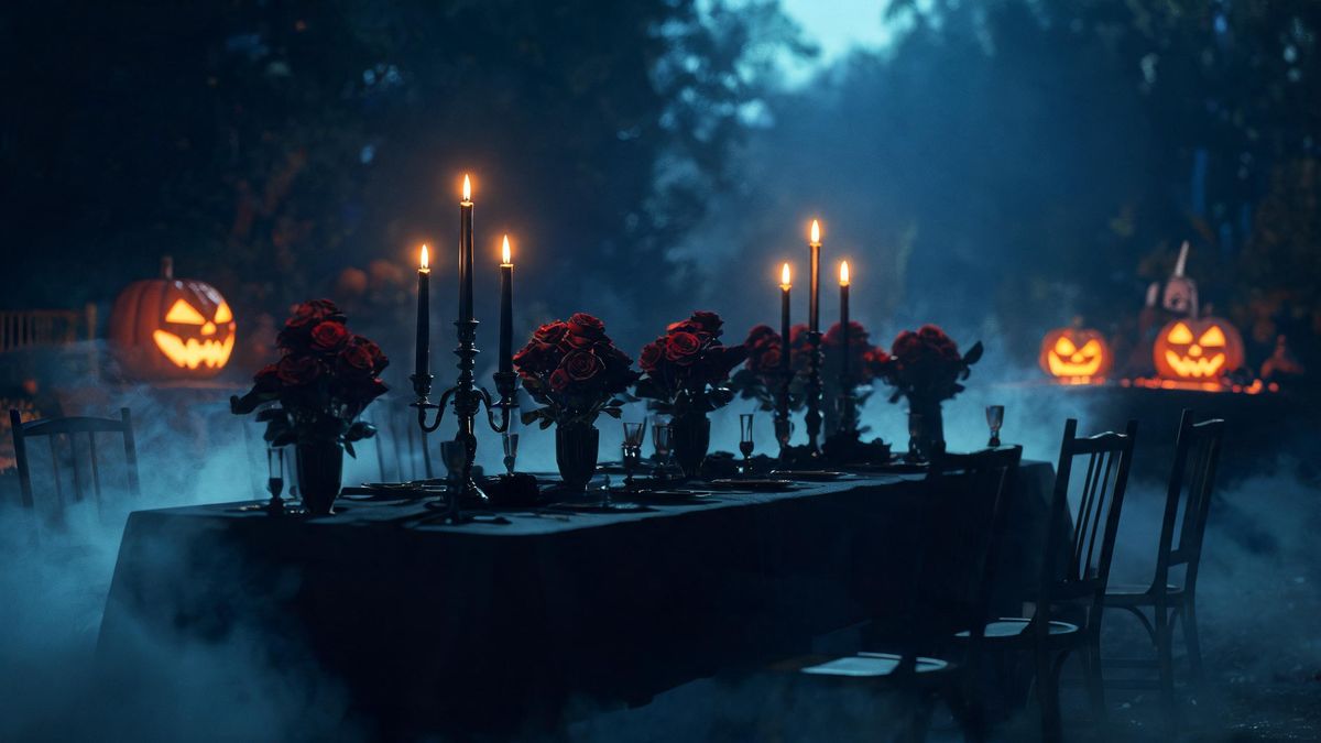 A long dining table set with black candles and dark red roses, no people, candlelight only