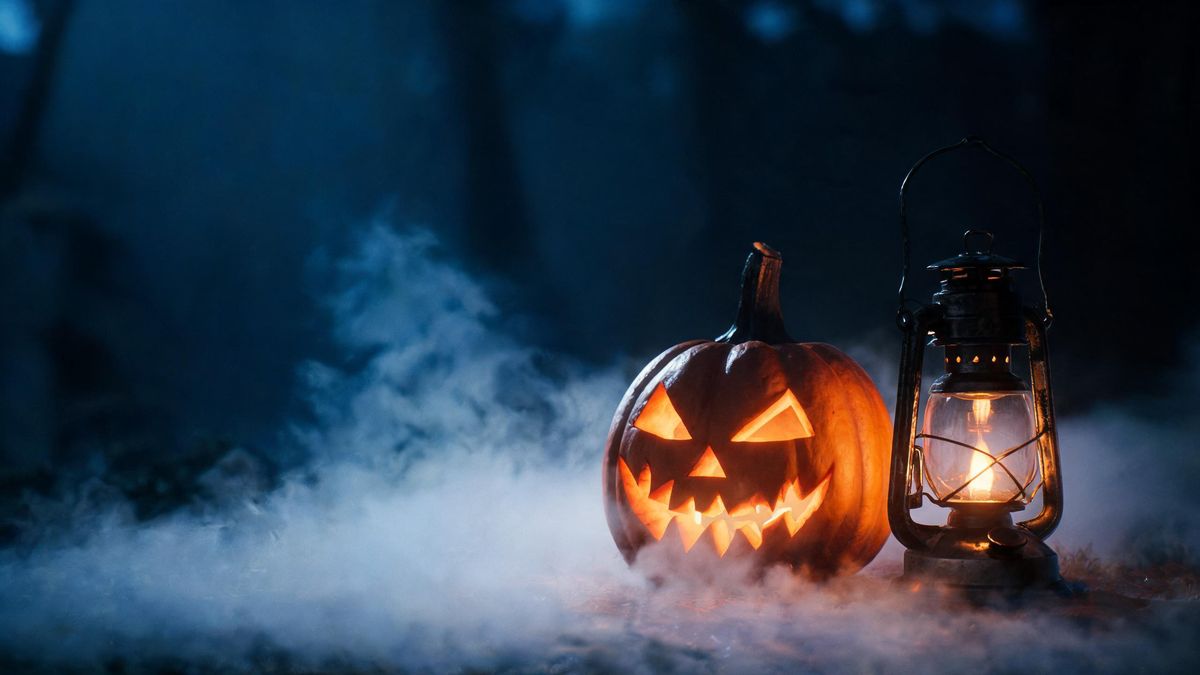 A still life of a carved pumpkin and an oil lantern in low fog against a dark background